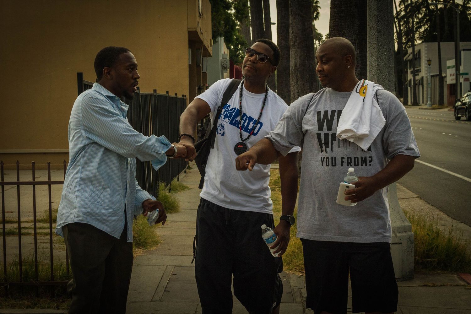 Three men stand on a city sidewalk engaged in animated conversation and laughter.
