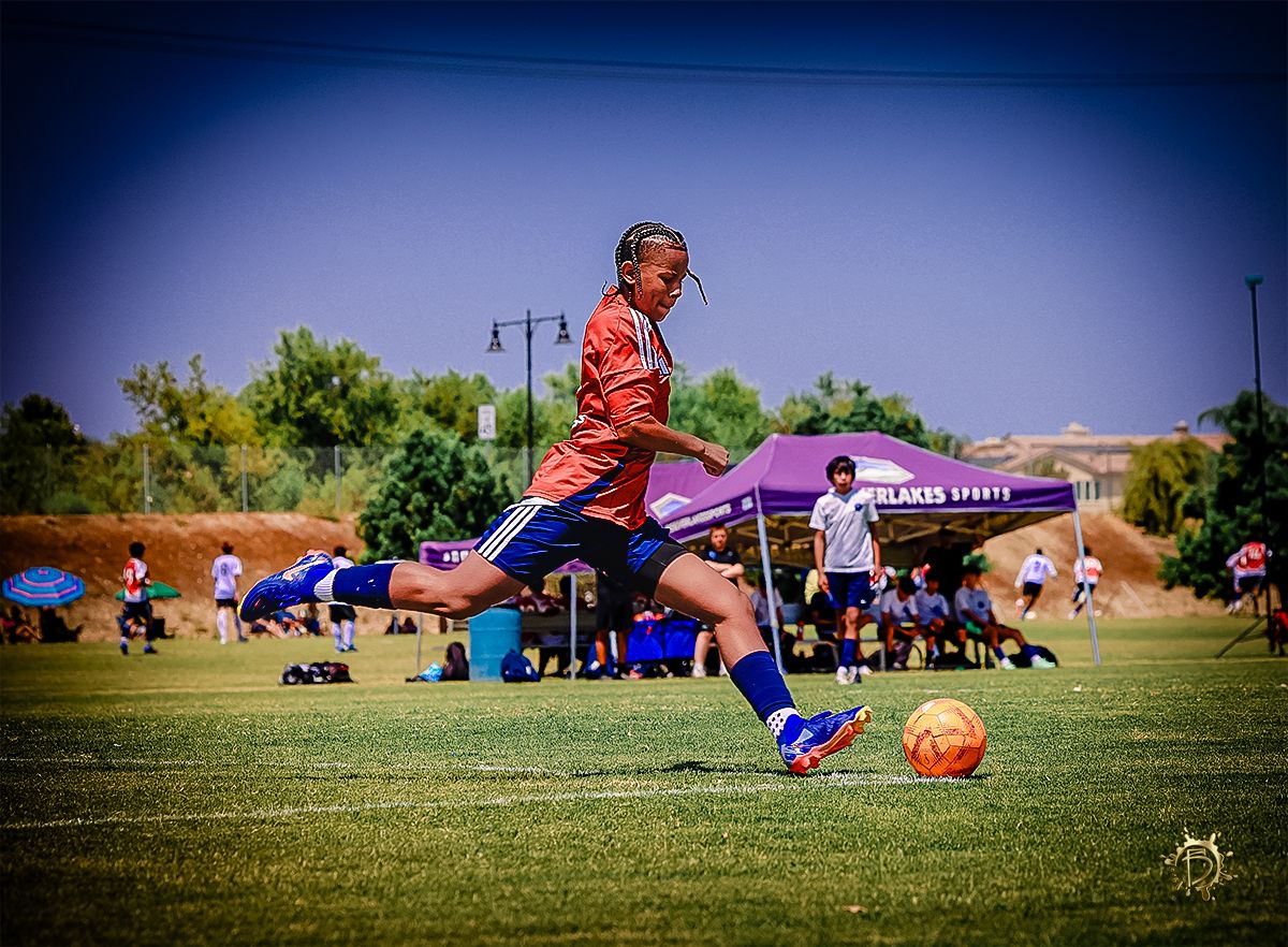 Soccer player slides to kick orange ball on green grass field during daytime match.