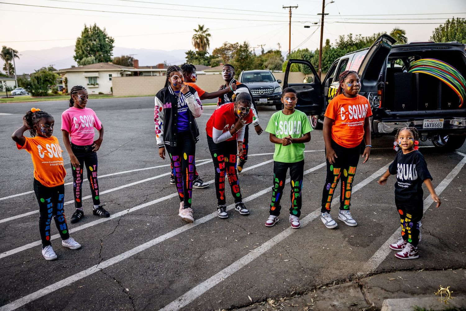 A group of people in colorful athletic wear stand in formation on an outdoor parking lot during a fitness activity.