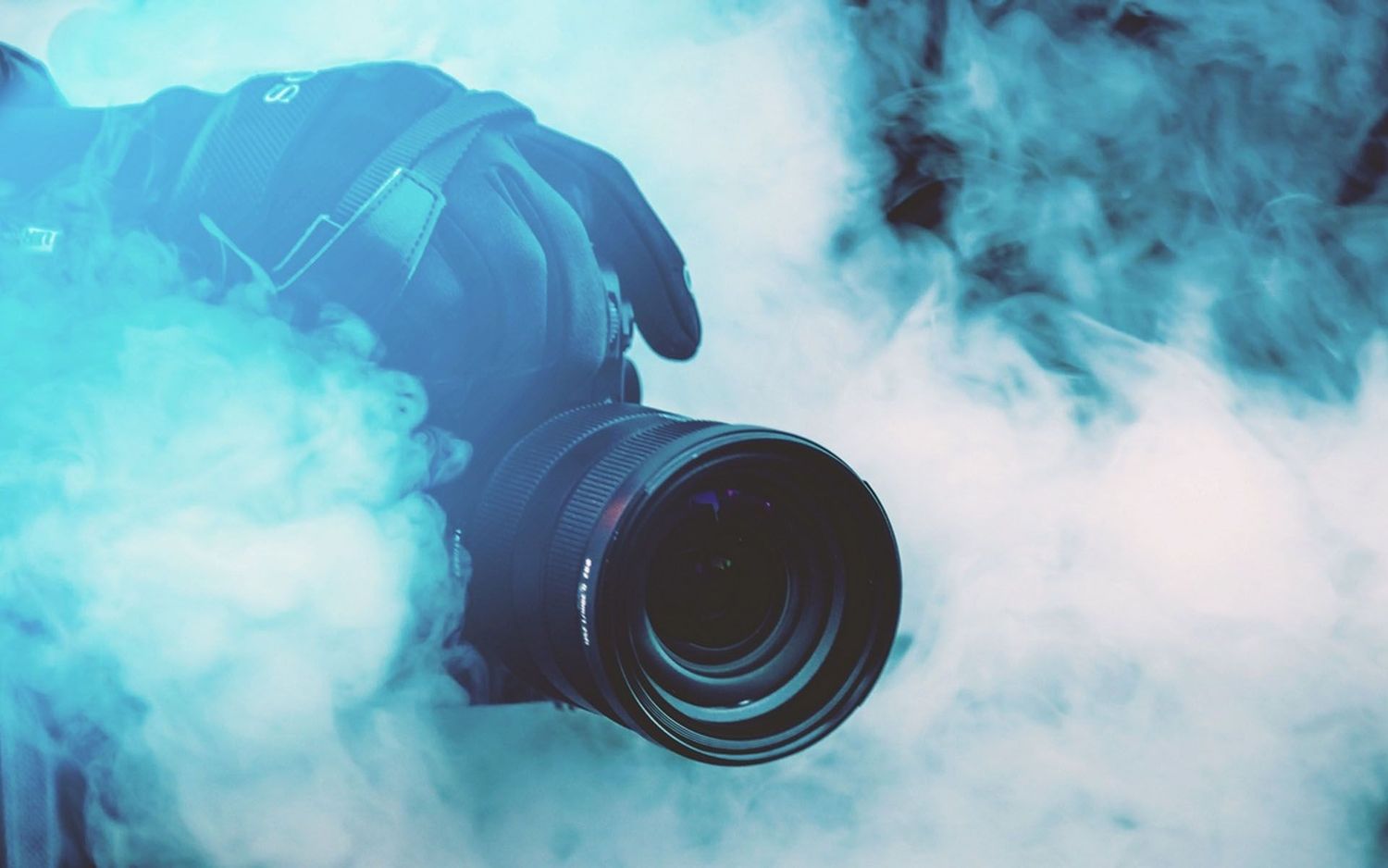 A camera lens surrounded by ethereal blue smoke or fog creates a mysterious atmospheric photography effect.