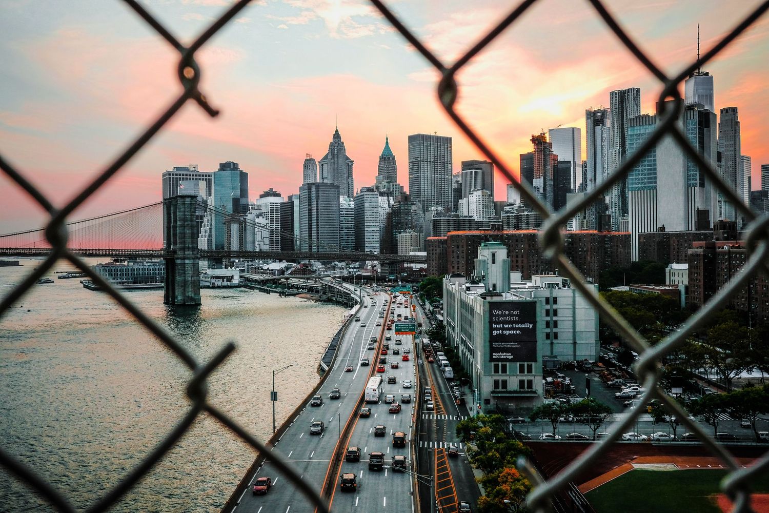 Manhattan skyline and FDR Drive highway seen through chain link fence during sunset in New York City.
