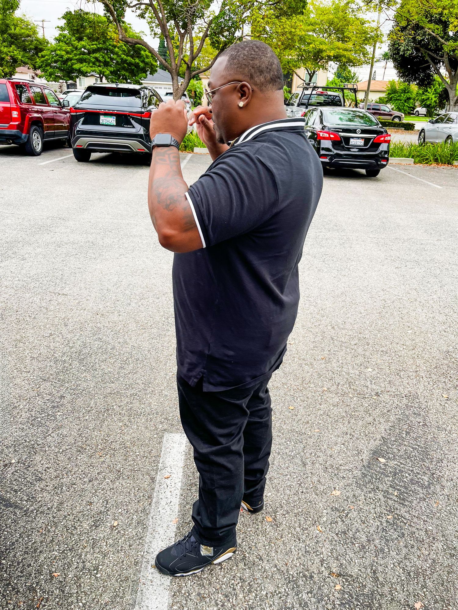 A person in dark clothing photographing something with a mobile phone in a parking lot with trees in the background.