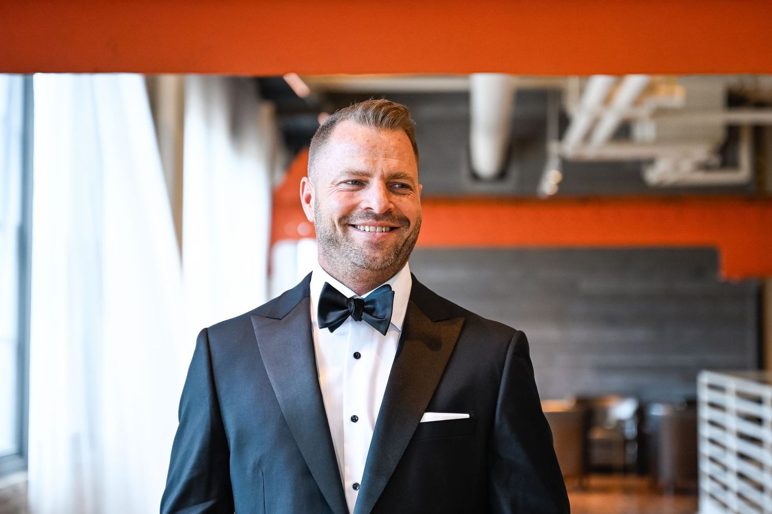 Person in formal attire standing in venue with orange walls and wooden floors.