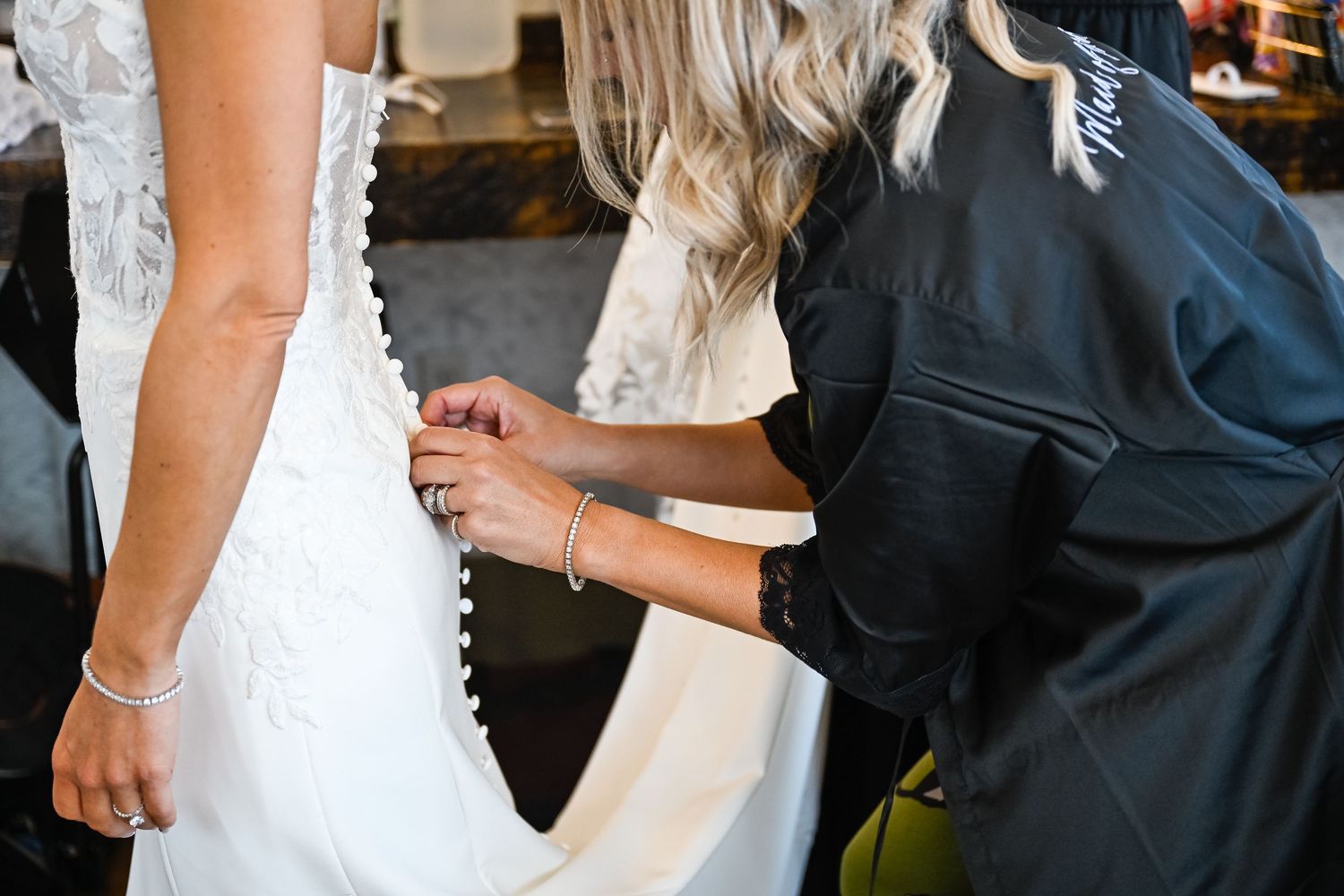 Bride in white lace dress and groom in dark suit embrace during first look wedding moment.