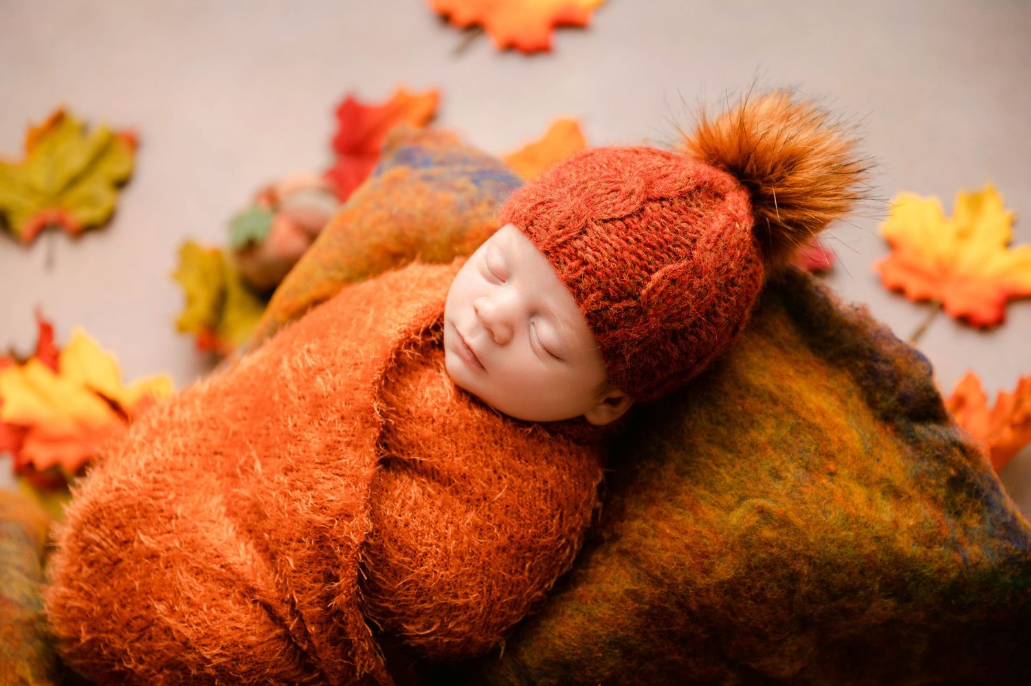 A brown teddy bear sits nestled among colorful autumn leaves and orange pumpkins in a seasonal fall display.