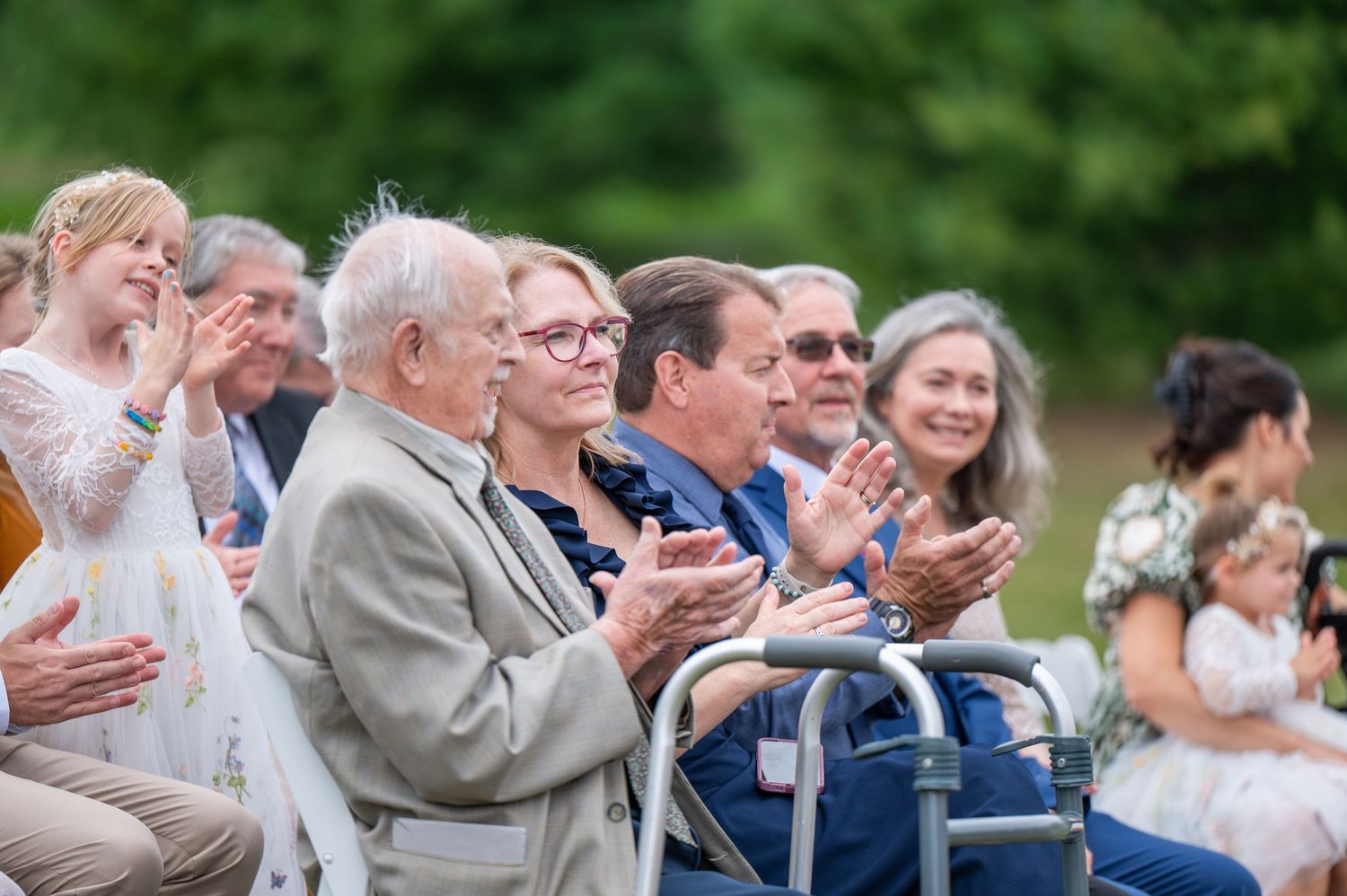 Wedding guests sitting outdoors smile and applaud during an emotional outdoor ceremony.