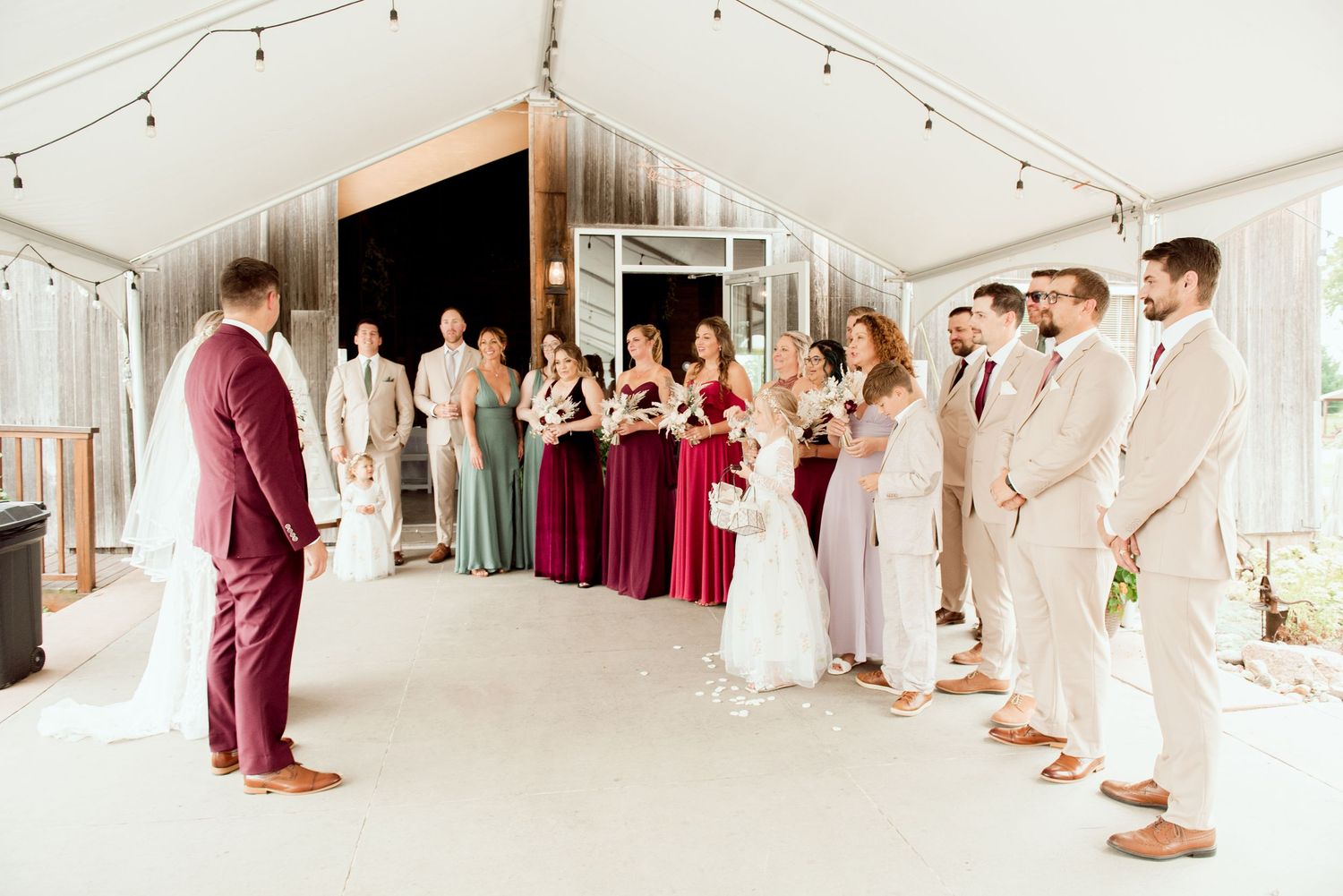 Wedding party gathers inside a modern white barn venue with string lights and elegant decor.