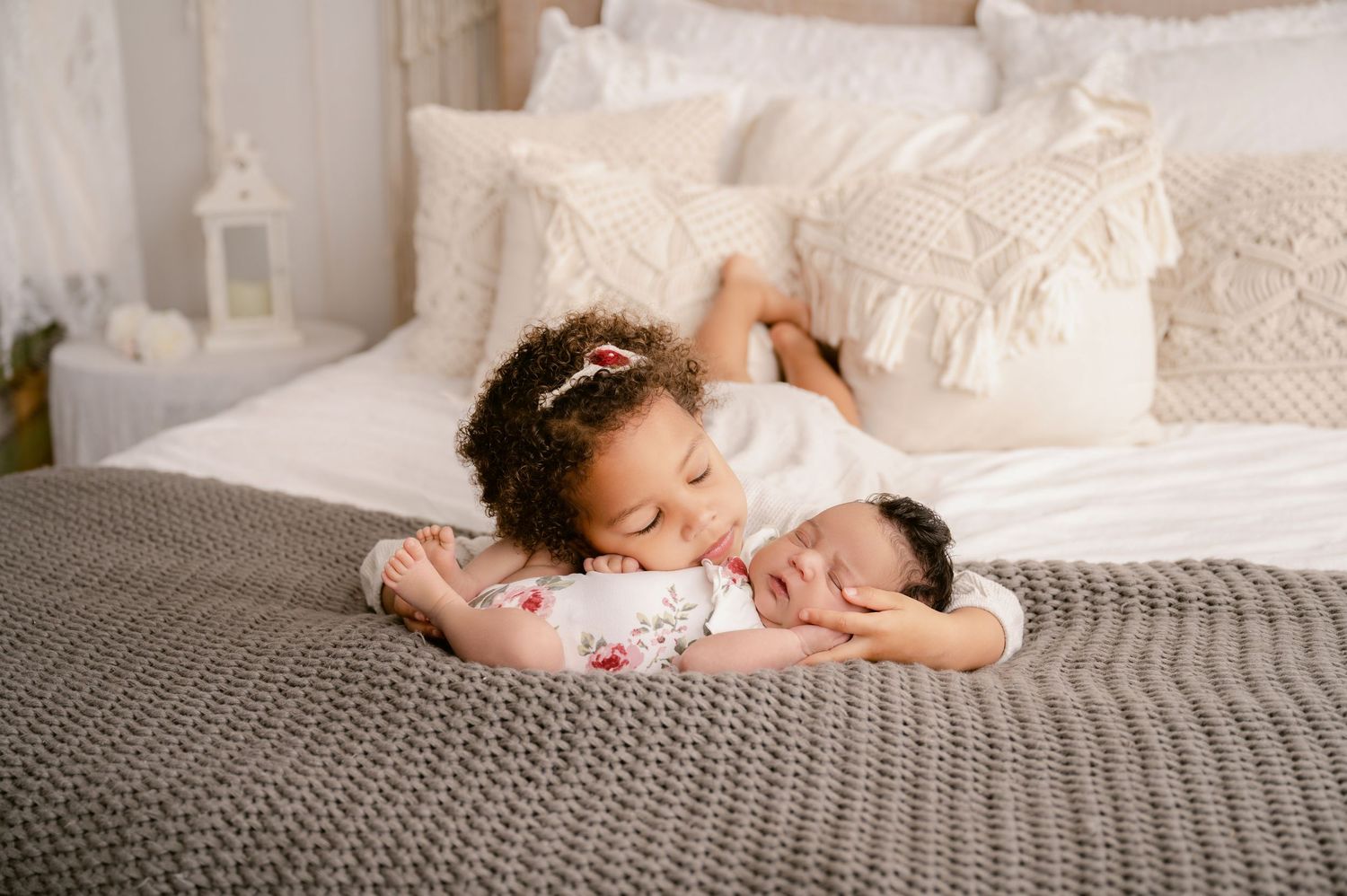 St Cloud newborn Photos of Young girl lovingly kisses newborn sibling while lying on a cozy bed with white bedding.