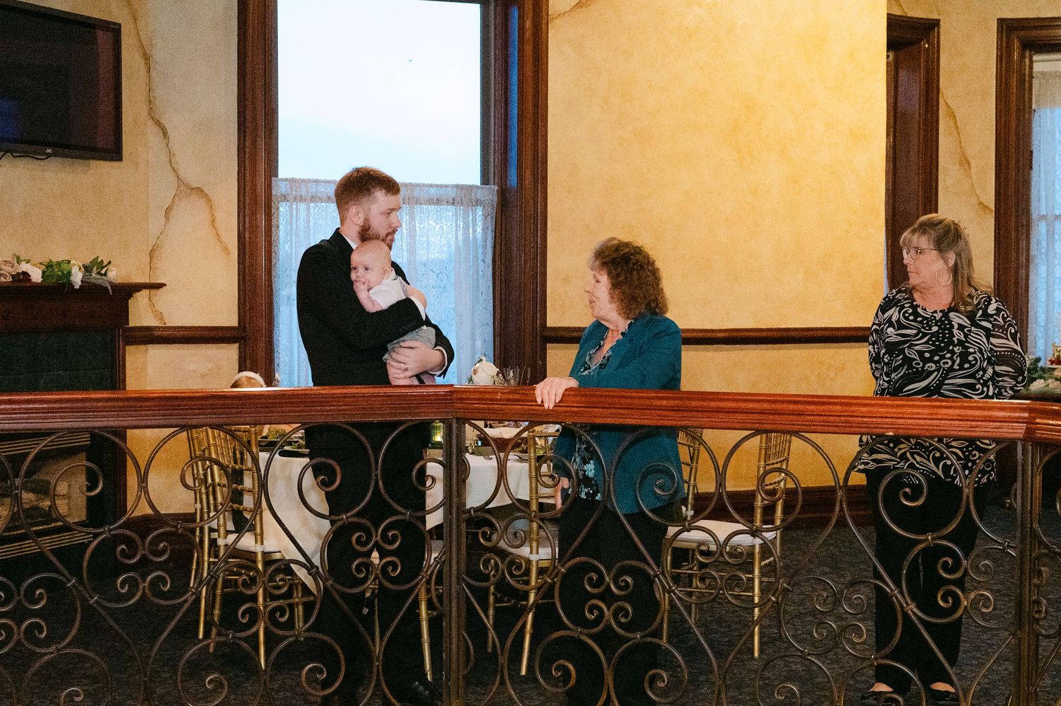 Central MN Wedding Photos | Three guests conversing at ornate iron railing in elegant reception venue.