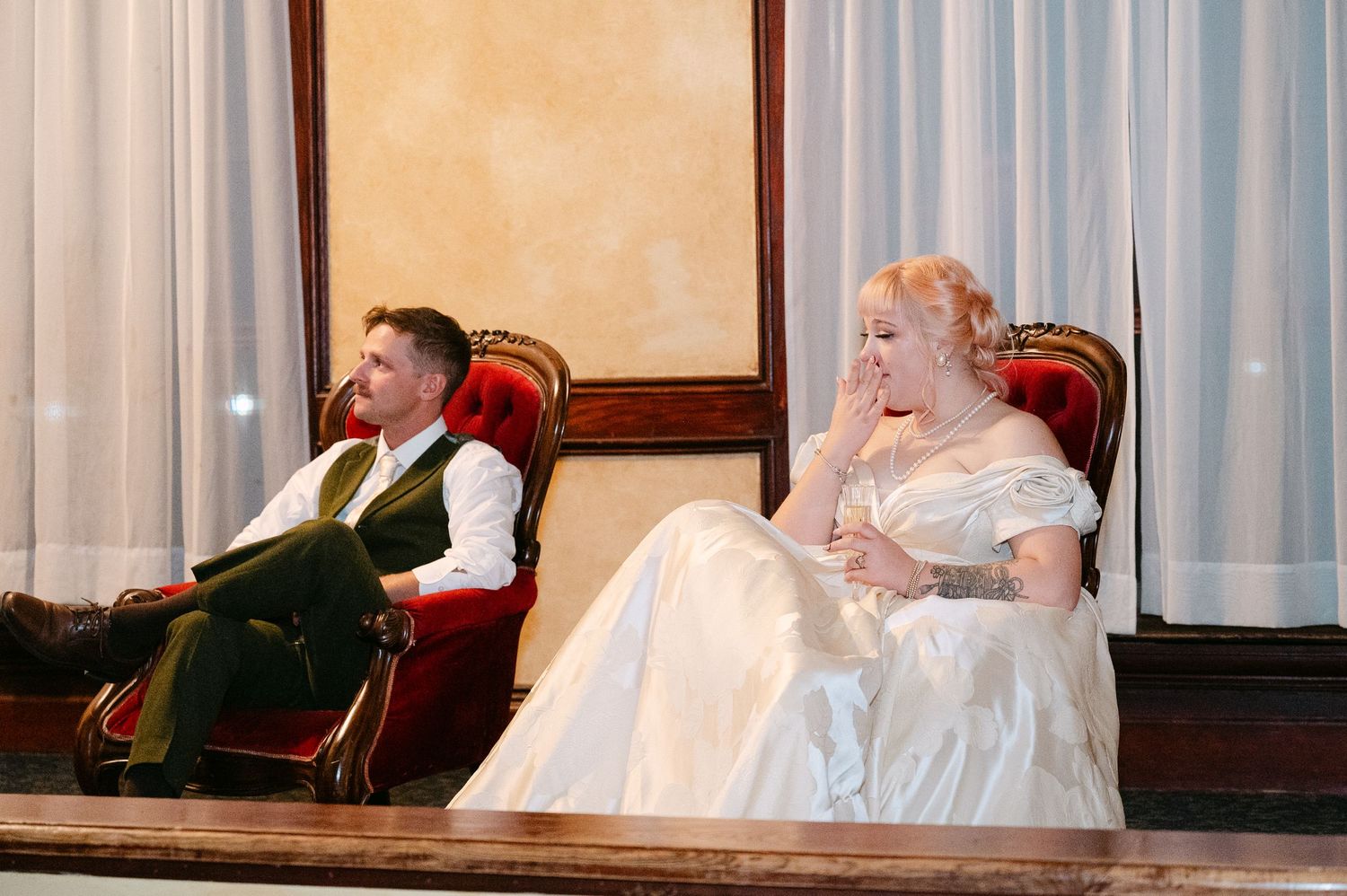 Central MN Wedding Photos | Bride and groom sit in ornate red chairs during wedding reception festivities.