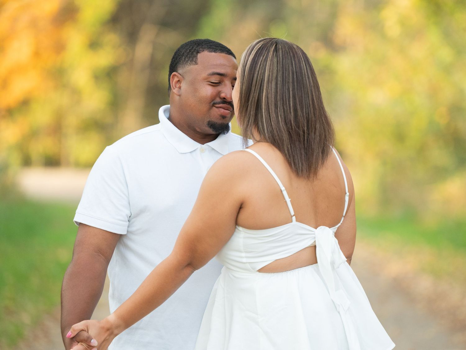Central Minnesota Best Engagement Photographer -Couple in matching white outfits holding hands on a scenic autumn path with colorful foliage