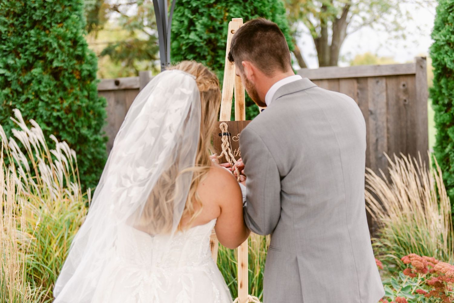 Central MN Wedding Photos - Bride and groom pray together at rustic wooden cross during outdoor wedding ceremony.