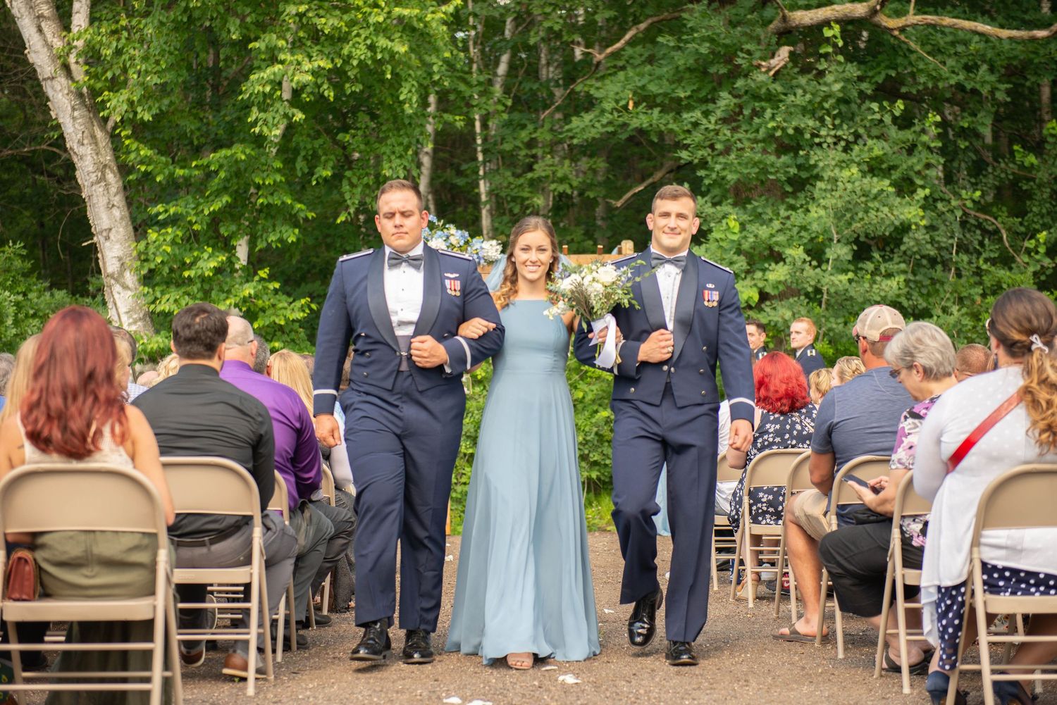 Wedding party in navy and light blue attire proceed down outdoor forest path. Zimmerman MN Weddings