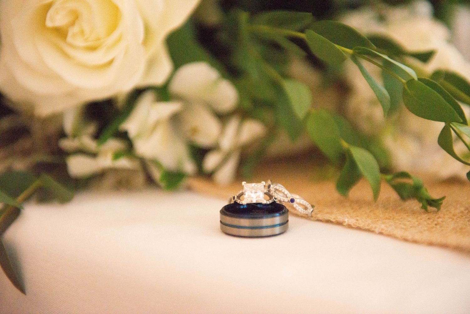 Wedding rings displayed on textured bands against white floral and greenery decorations. Zimmerman MN Weddings