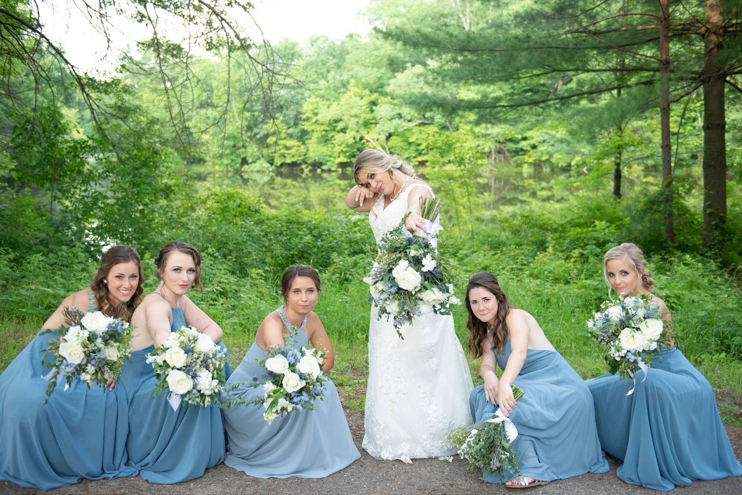 Bridesmaids in dusty blue dresses pose with bouquets against a forest backdrop. Zimmerman MN Weddings