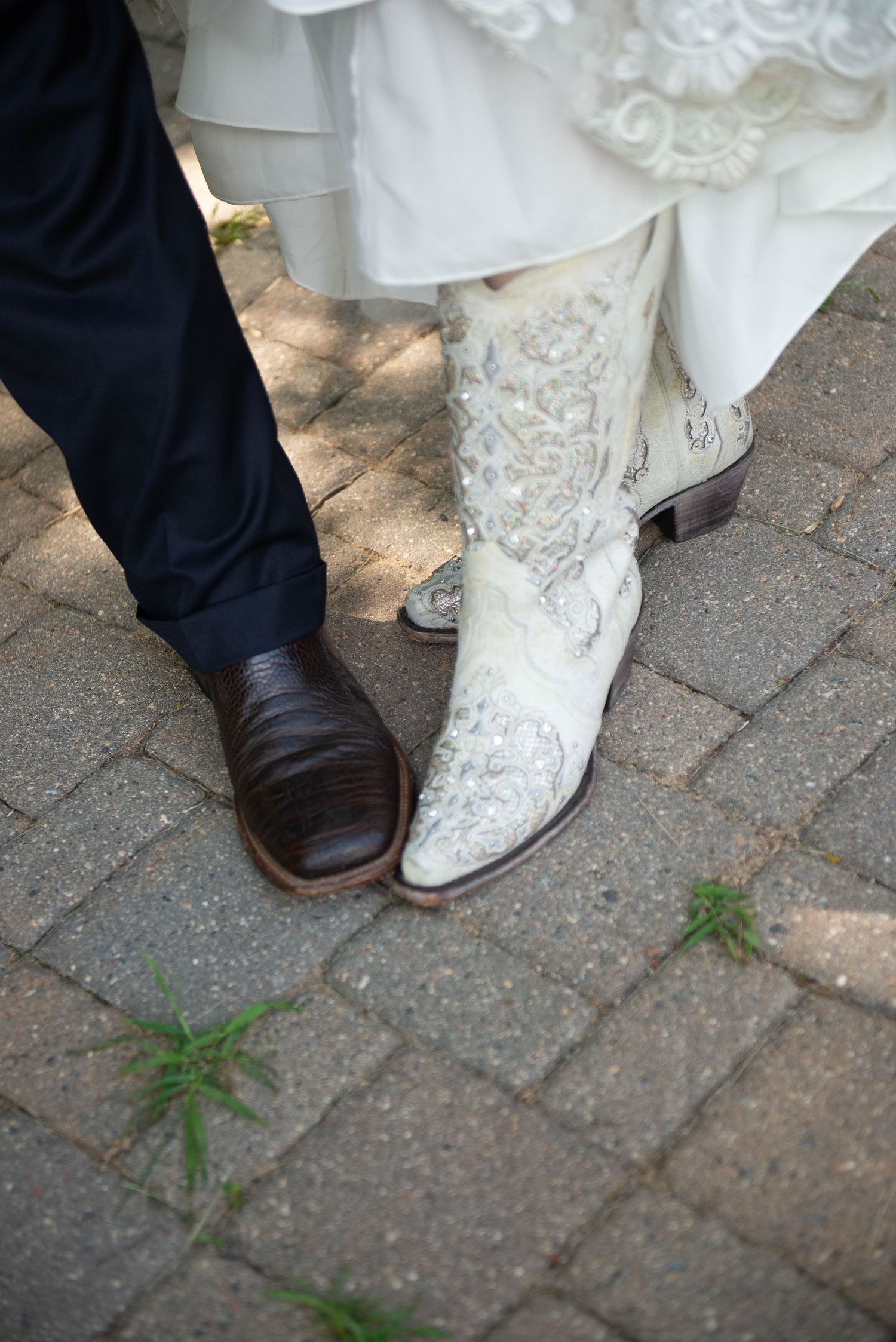 Contrasting footwear of wedding couple showing elegant dress shoe and embroidered white western boot on brick pavers. Zimmerman MN Weddings