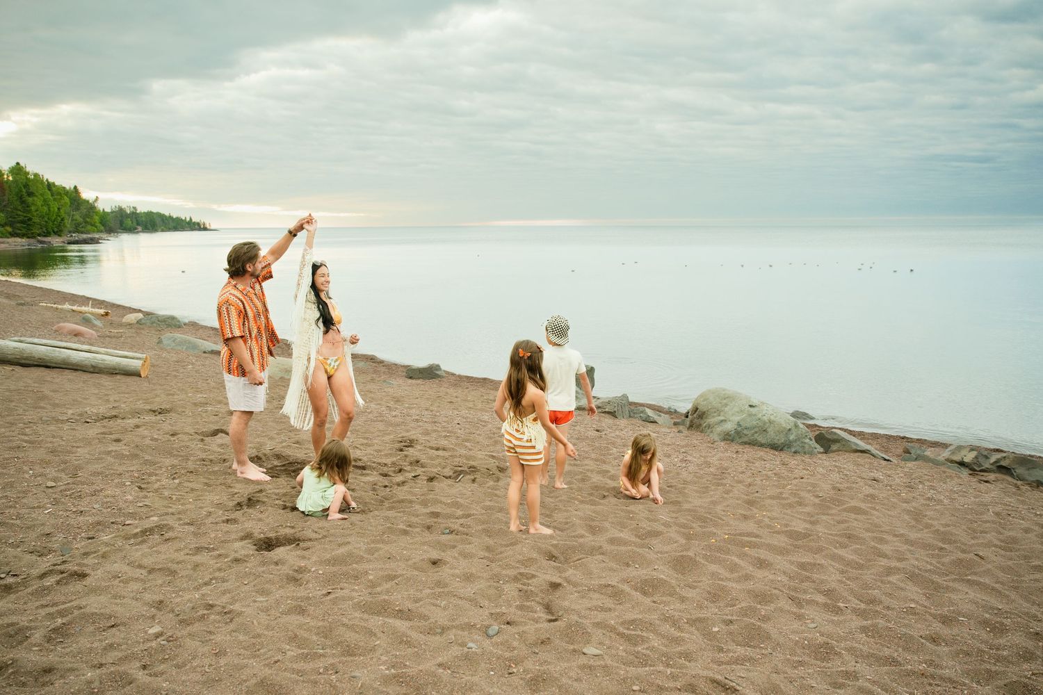 Family enjoying a peaceful beach evening, with children playing on sandy shore near calm water at dusk.