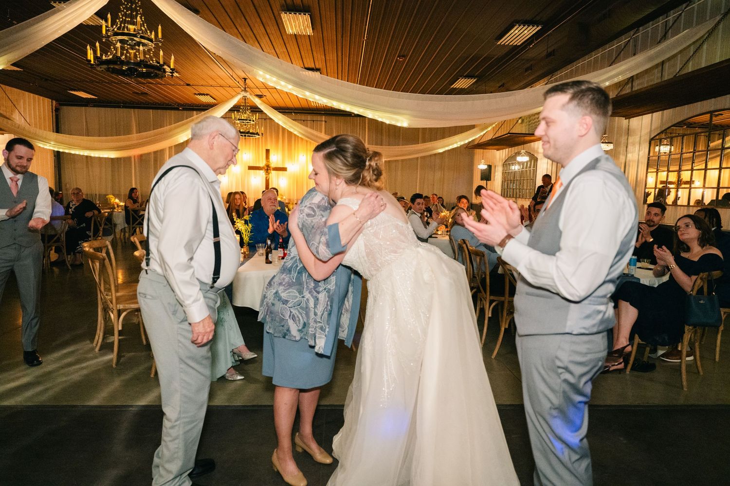 Bride hugs a family member during a parent dance at the wedding reception in a barn venue.