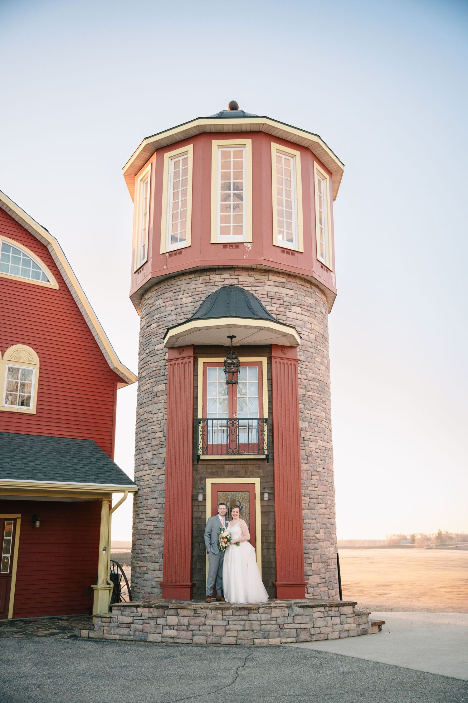 Bride and groom pose together in front of a charming red stone tower at their wedding venue.