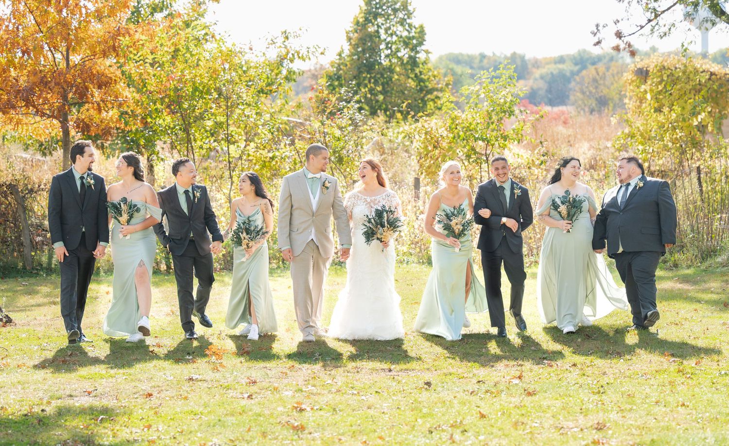 Wedding party walks outdoors in fall foliage wearing mint bridesmaid dresses and grey suits.