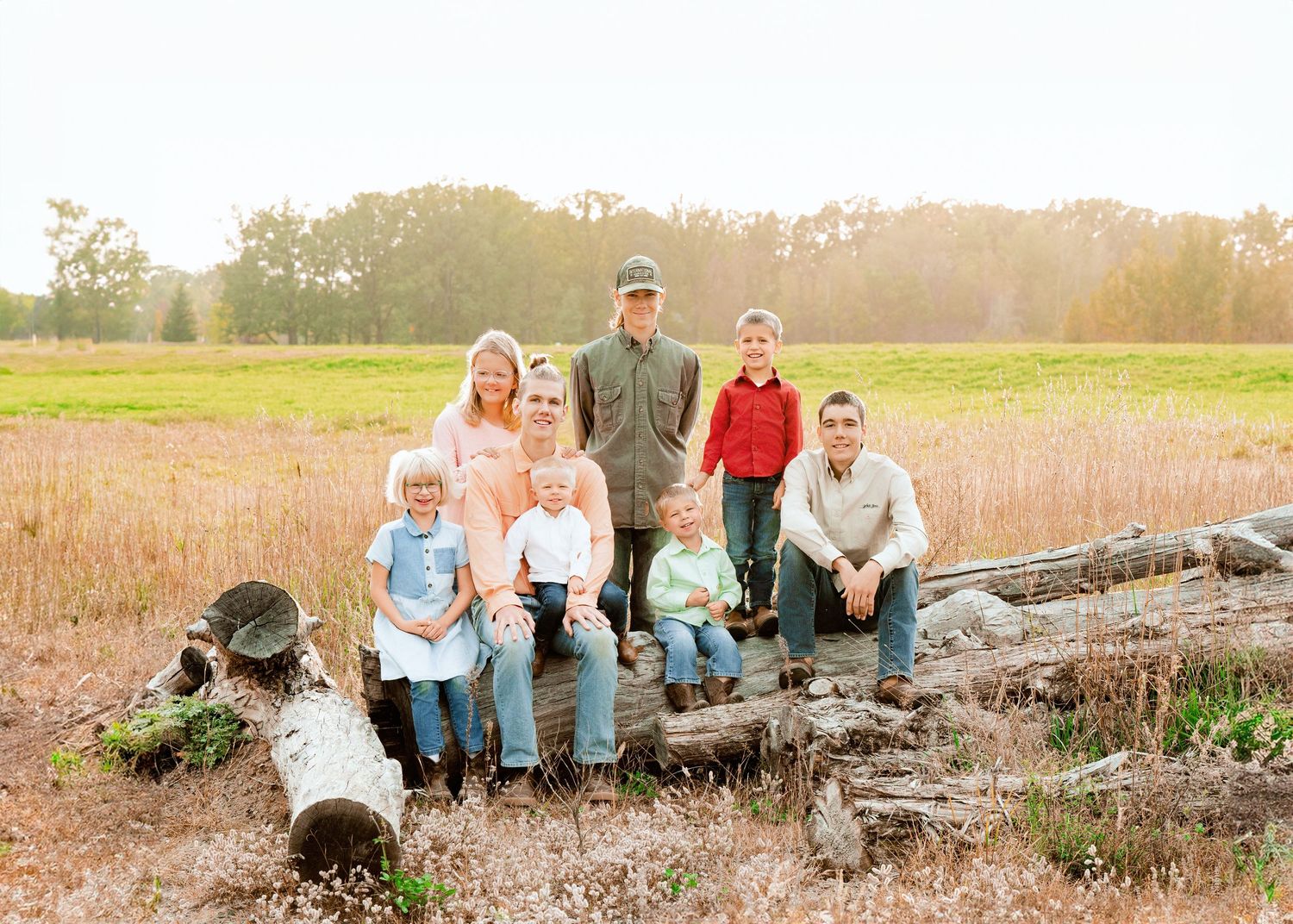 A group poses outdoors on a fallen log in a golden field at sunset.