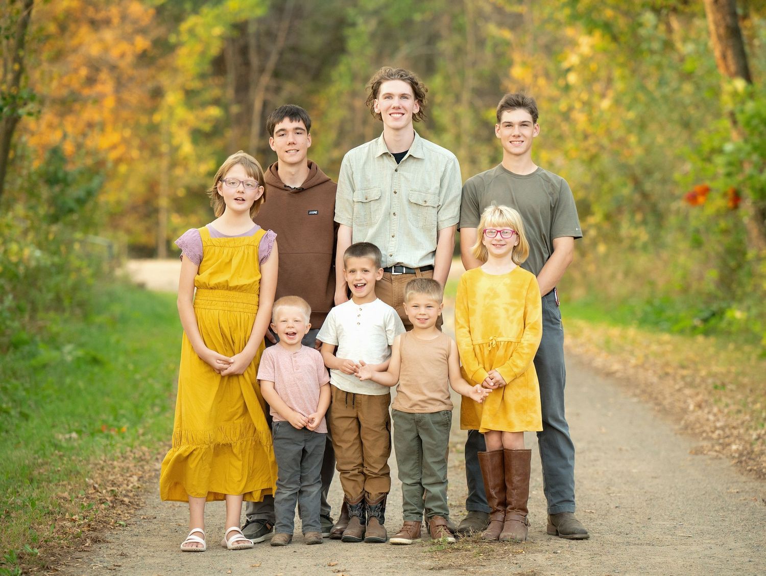 A group of people wearing coordinated casual outfits stand together on a tree-lined autumn path.