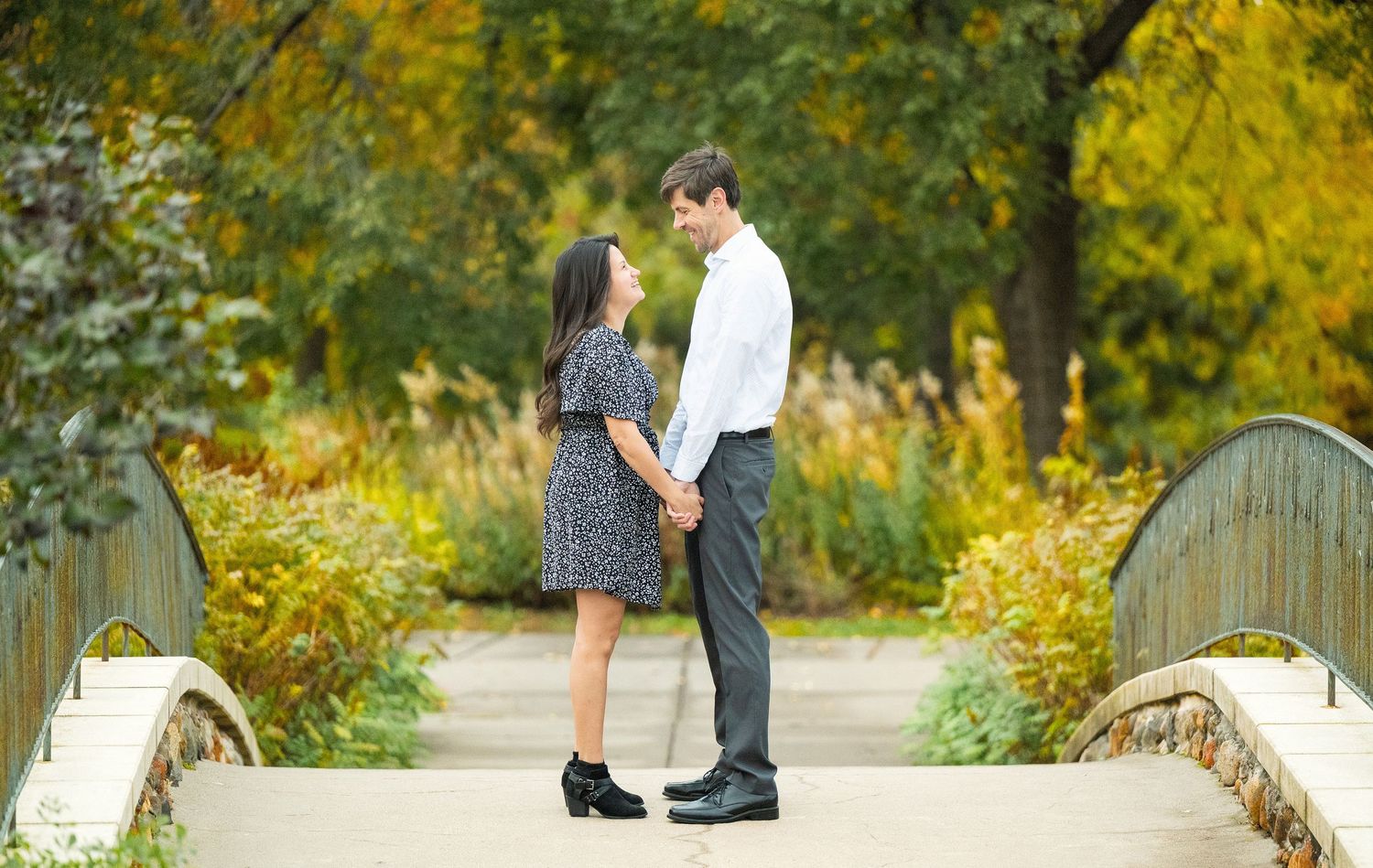 A couple shares romantic moments along a wooden bridge surrounded by autumn foliage at Lake Como. Engagement Sessions Minnesota.