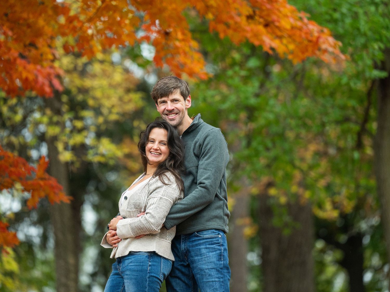A couple shares an intimate moment outdoors surrounded by vibrant orange and red autumn leaves at Lake Como. Engagement Sessions Minnesota.