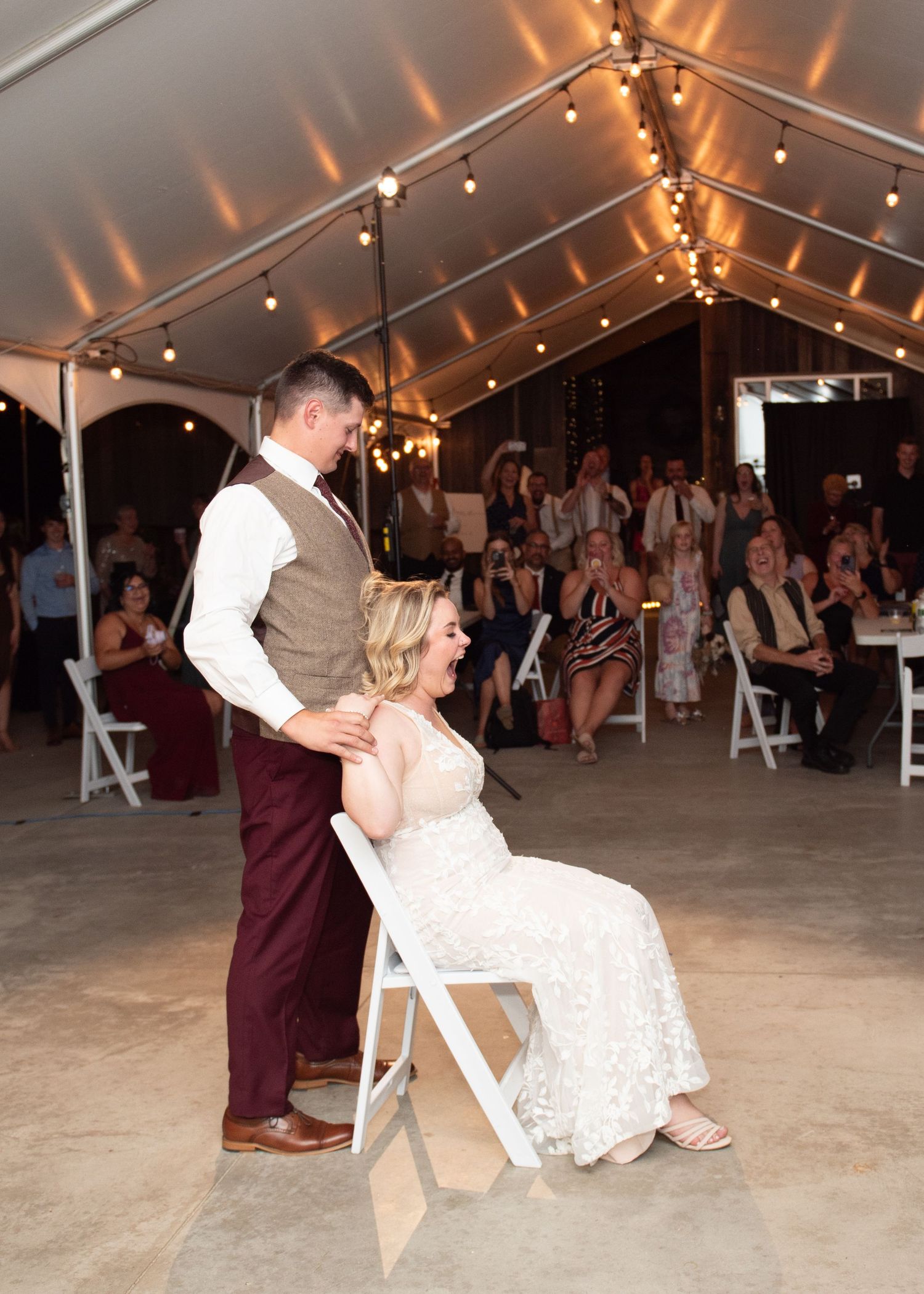 A bride and groom share a special moment during their reception under a tent with string lights.