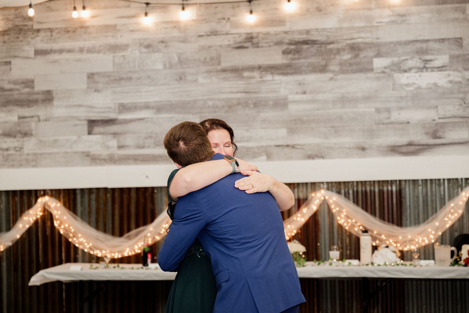 A rustic wedding venue interior with exposed wooden beams and a string of glowing lights illuminating the space.