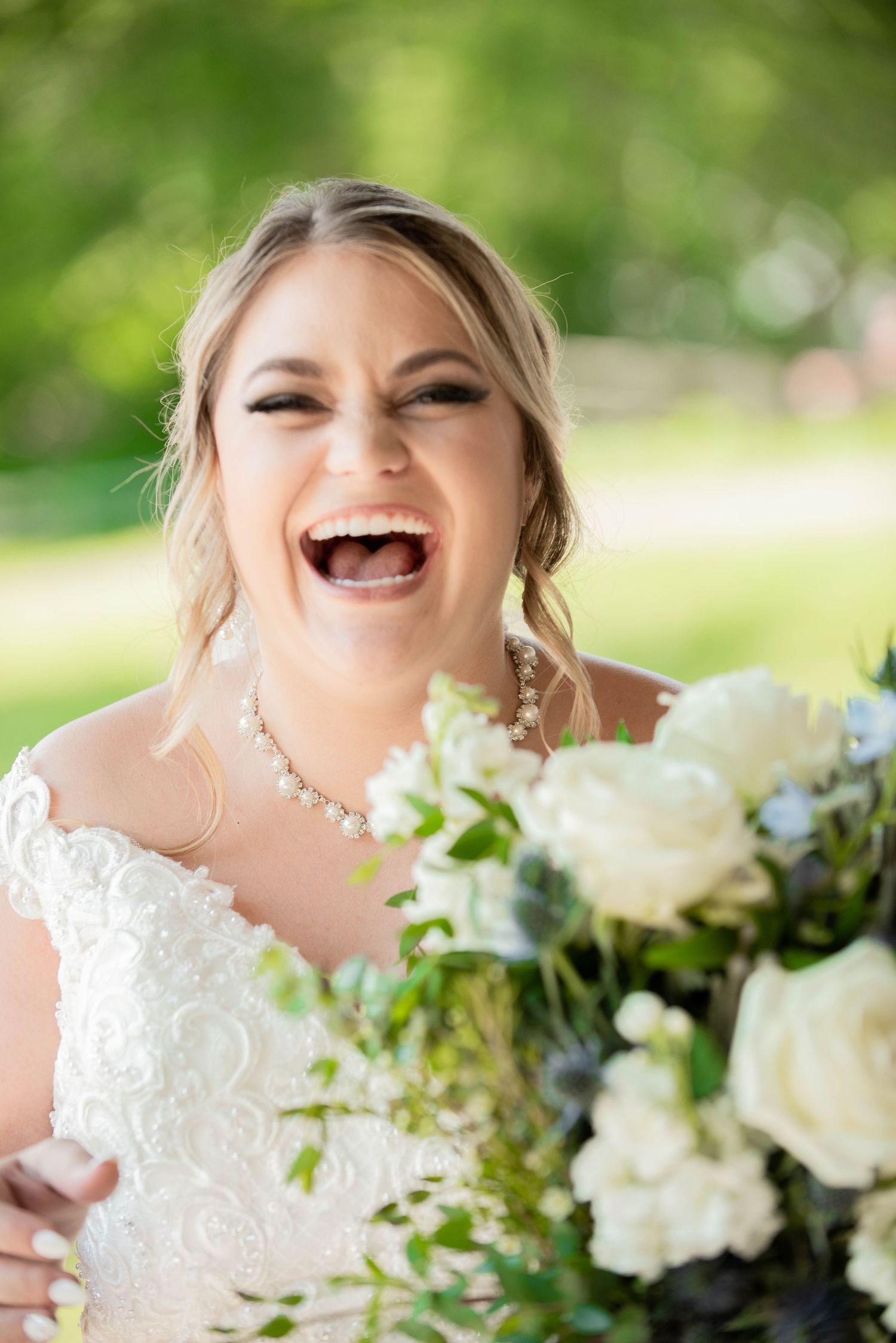 Bride holding a beautiful white floral bouquet against lush green foliage. Zimmerman MN Weddings