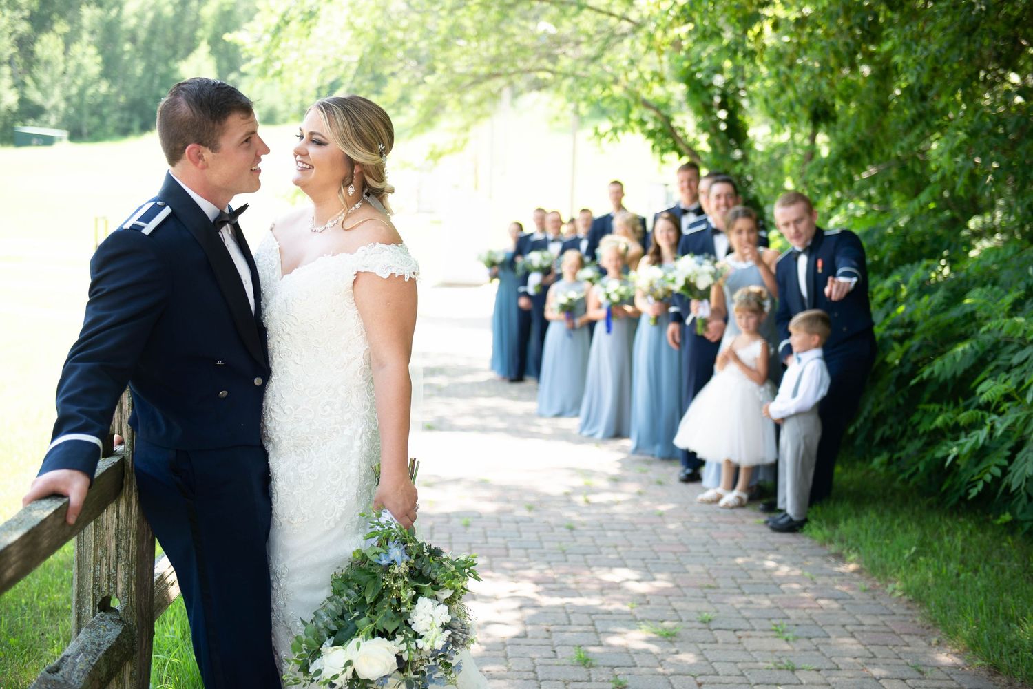 Wedding party lined up along garden path with bridesmaids in blue dresses and flower girls in white. Zimmerman MN Weddings