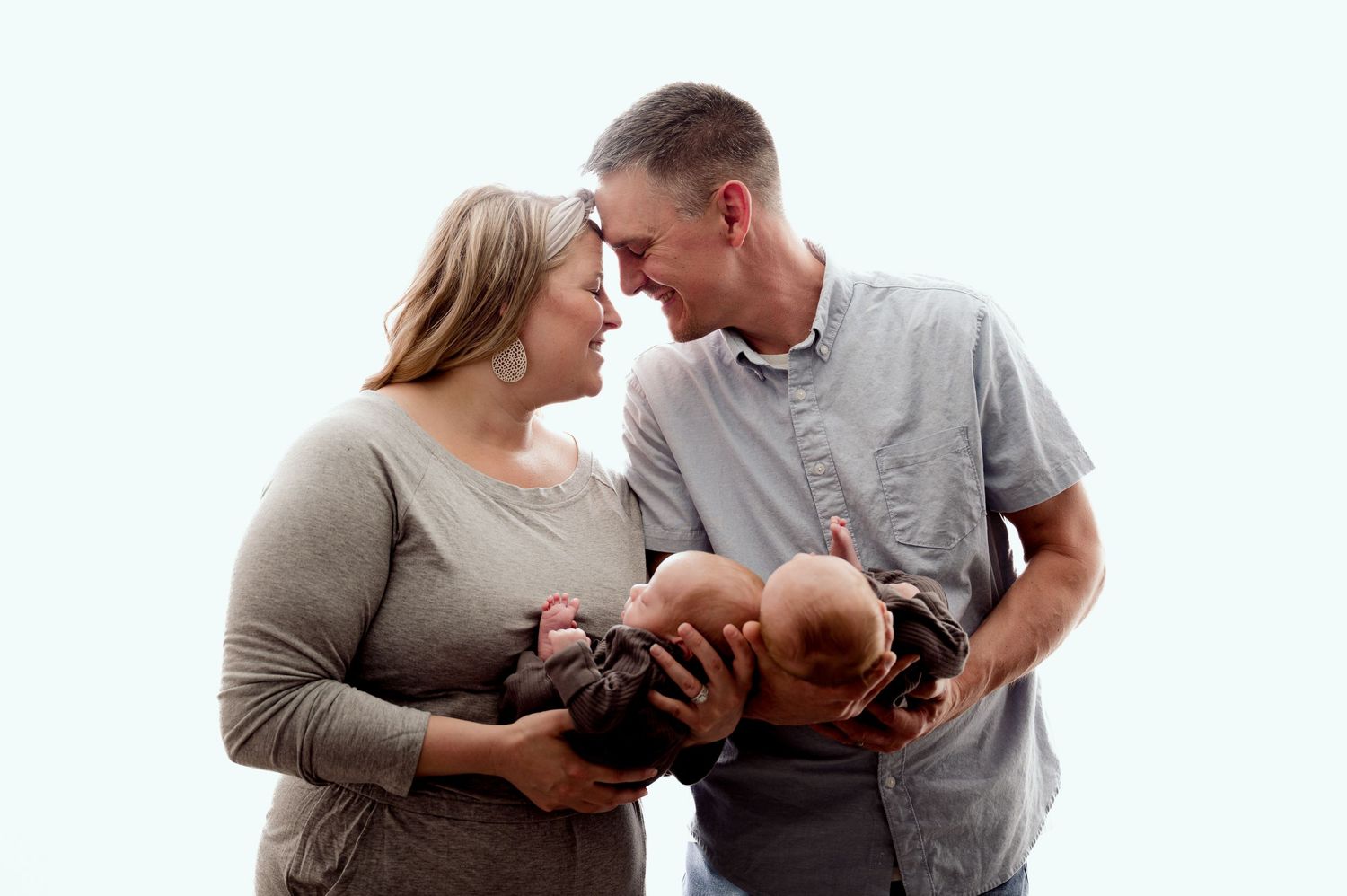 St Cloud newborn Photos of New parents lean foreheads together while cradling their newborn twins against a white background.