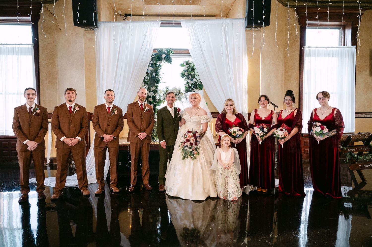 Central MN Wedding Photos | Wedding party poses together with bride in ball gown, groomsmen in brown suits, bridesmaids in burgundy.