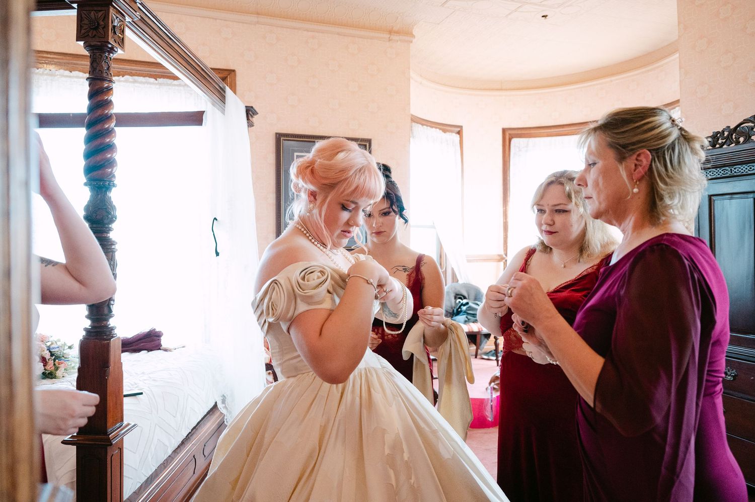 Central MN Wedding Photos | Bridesmaids in burgundy dresses helping bride into elegant champagne ball gown wedding dress before ceremony.