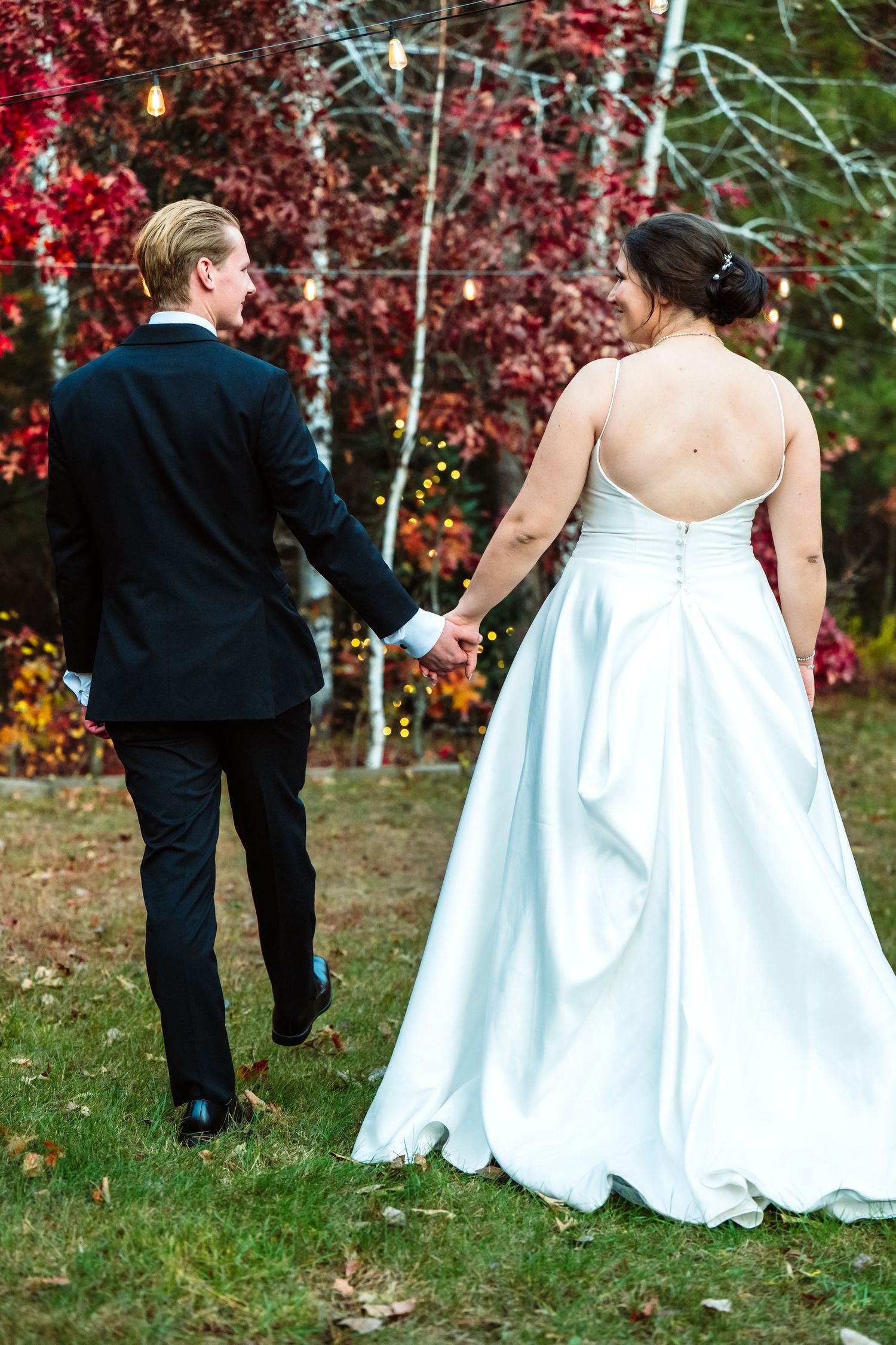 Wedding couple playfully running through autumn foliage with red maple trees in the background.