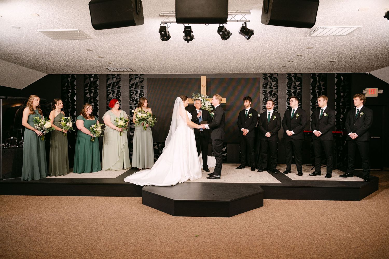 Wedding party lined up on stage during formal ceremony with decorative lighting backdrop.