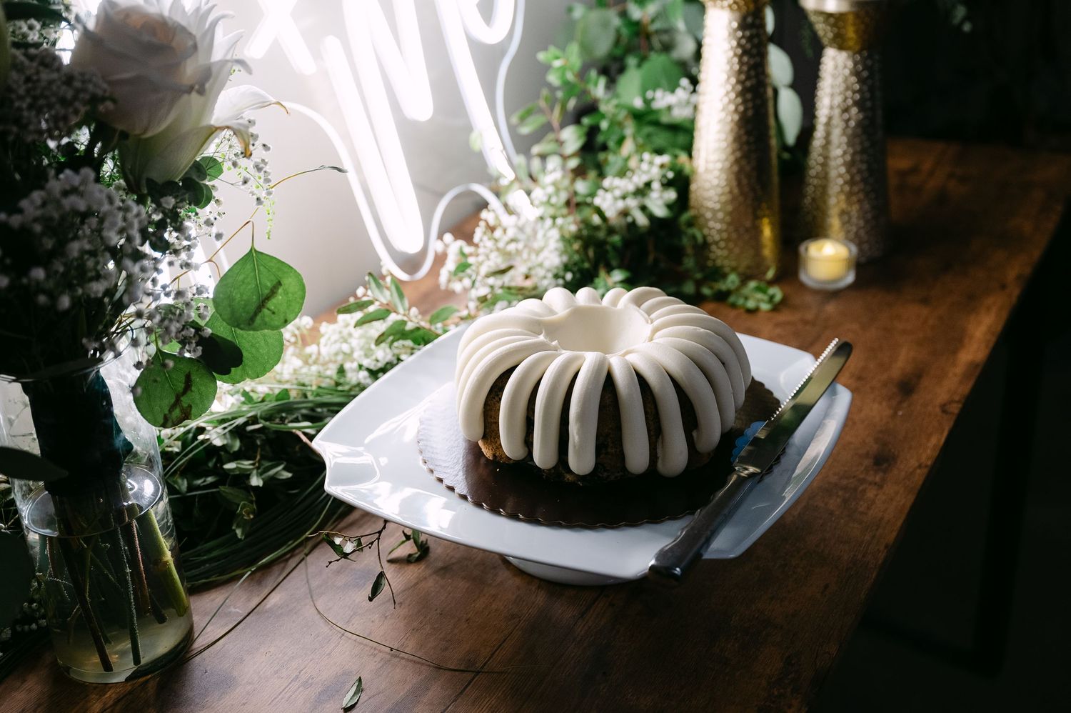 Rustic wedding reception table features greenery, white floral arrangements, and glowing candles on a wooden surface.