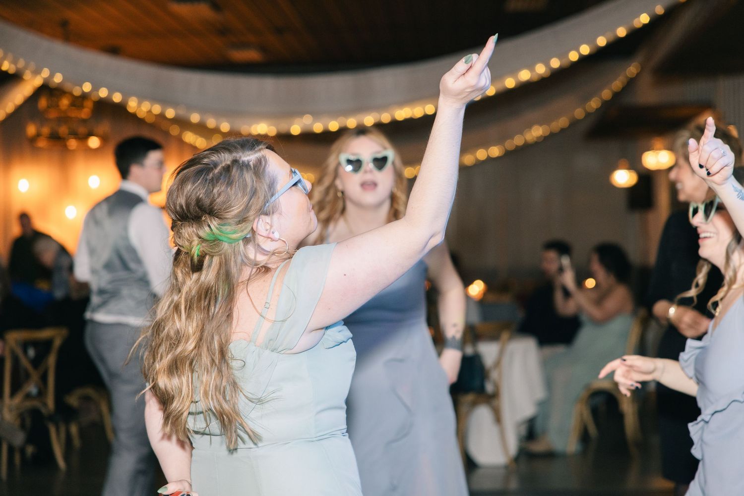 Bridesmaid dancing joyfully wearing fun novelty glasses at a lively wedding reception.