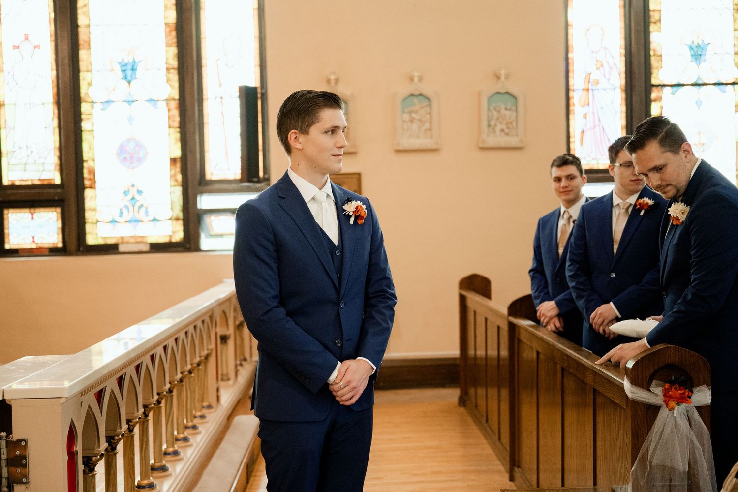 A groom in a navy blue suit stands at the altar while groomsmen gather in the church sanctuary.