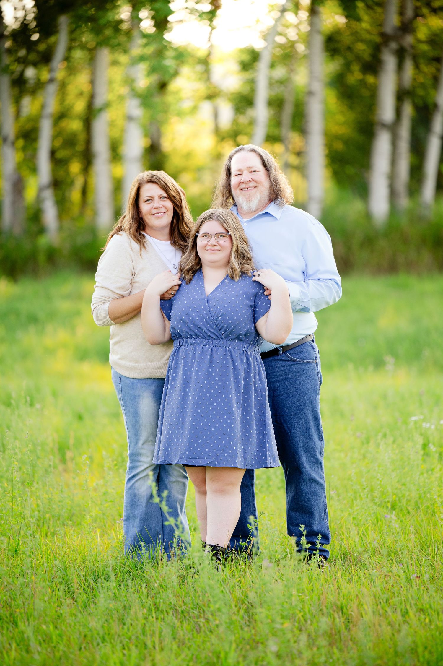 Family playfully posing together in a sunlit field with tall grass and trees in the background.