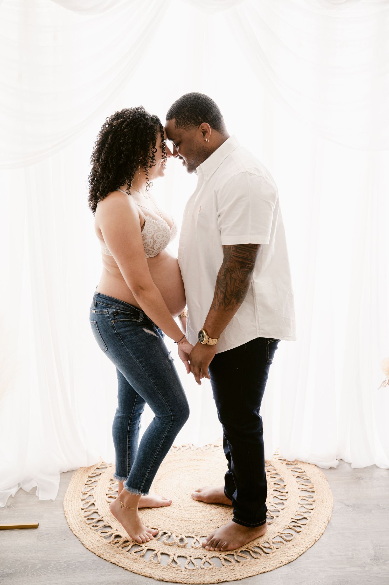 Two people in white and denim share intimate moments while dancing on a circular patterned rug in a bright studio.