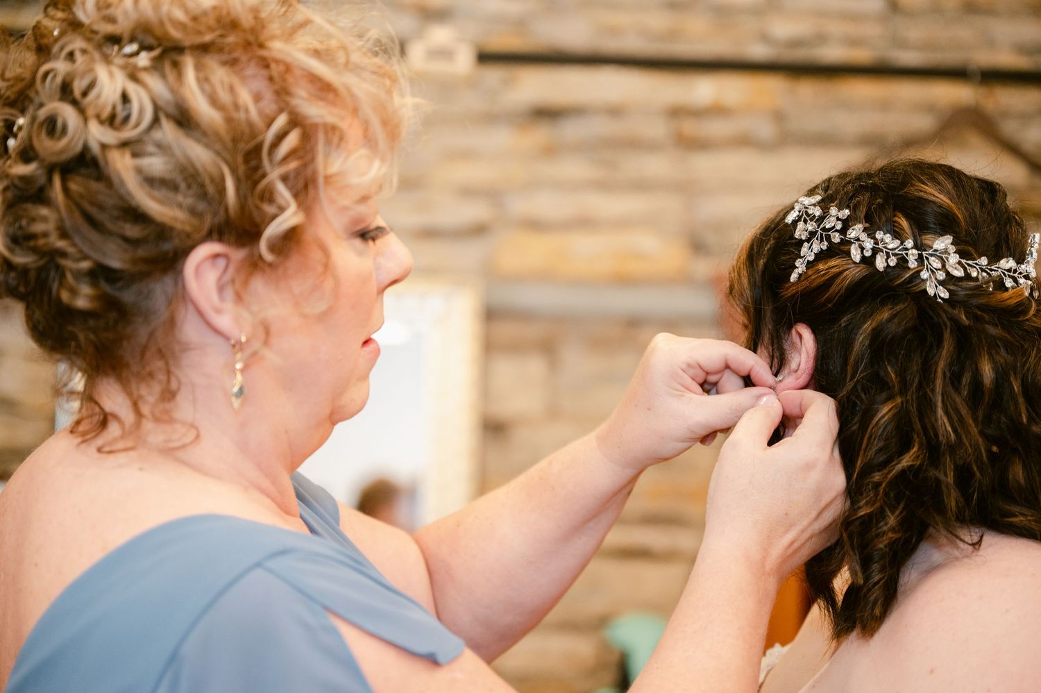 Central MN Wedding Photos - A woman helps a bride put on earrings before her wedding, both wearing elegant updos.