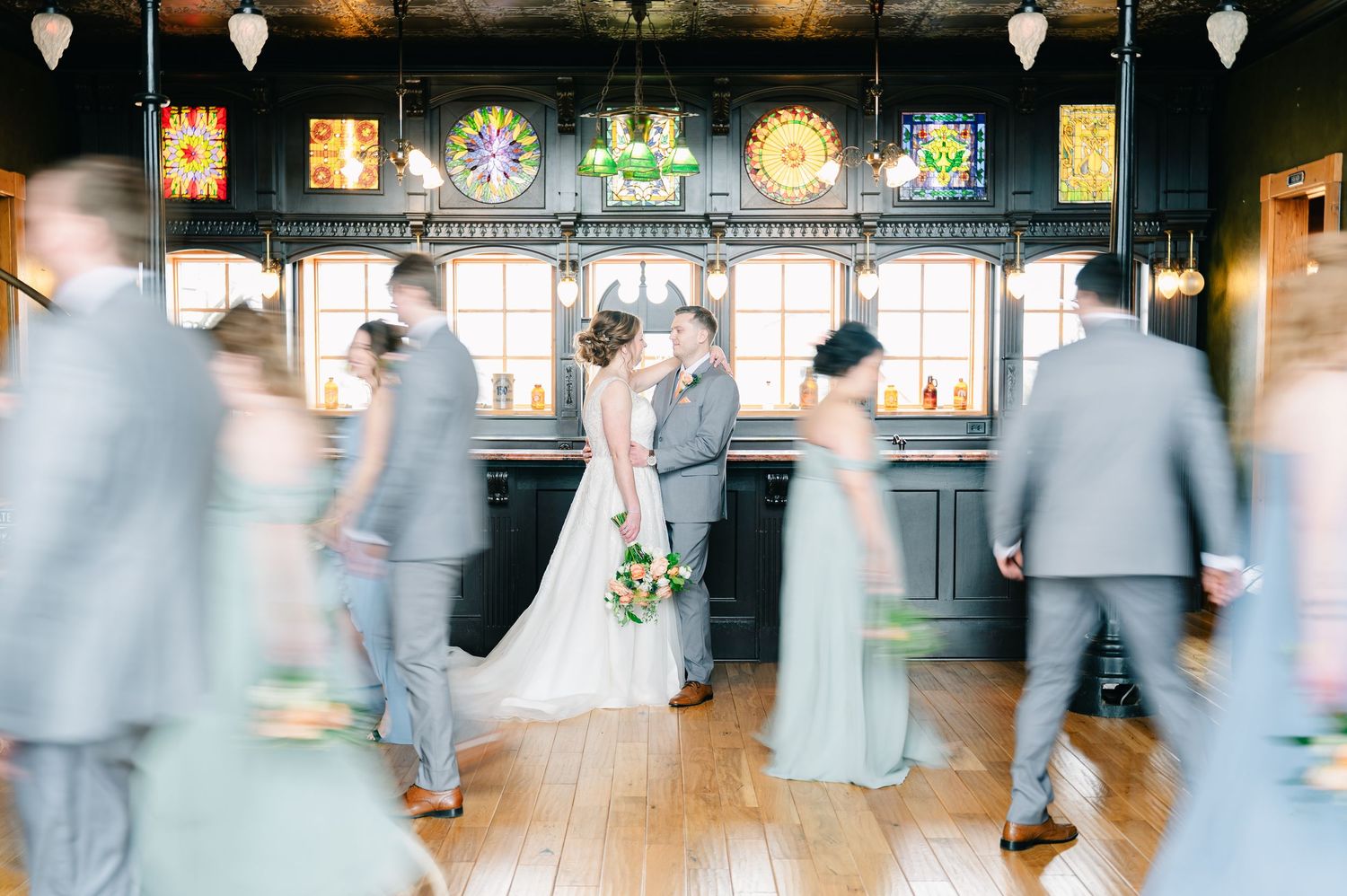 crooked willow weddings Wedding couple sharing a kiss surrounded by blurred bridal party in elegant venue.