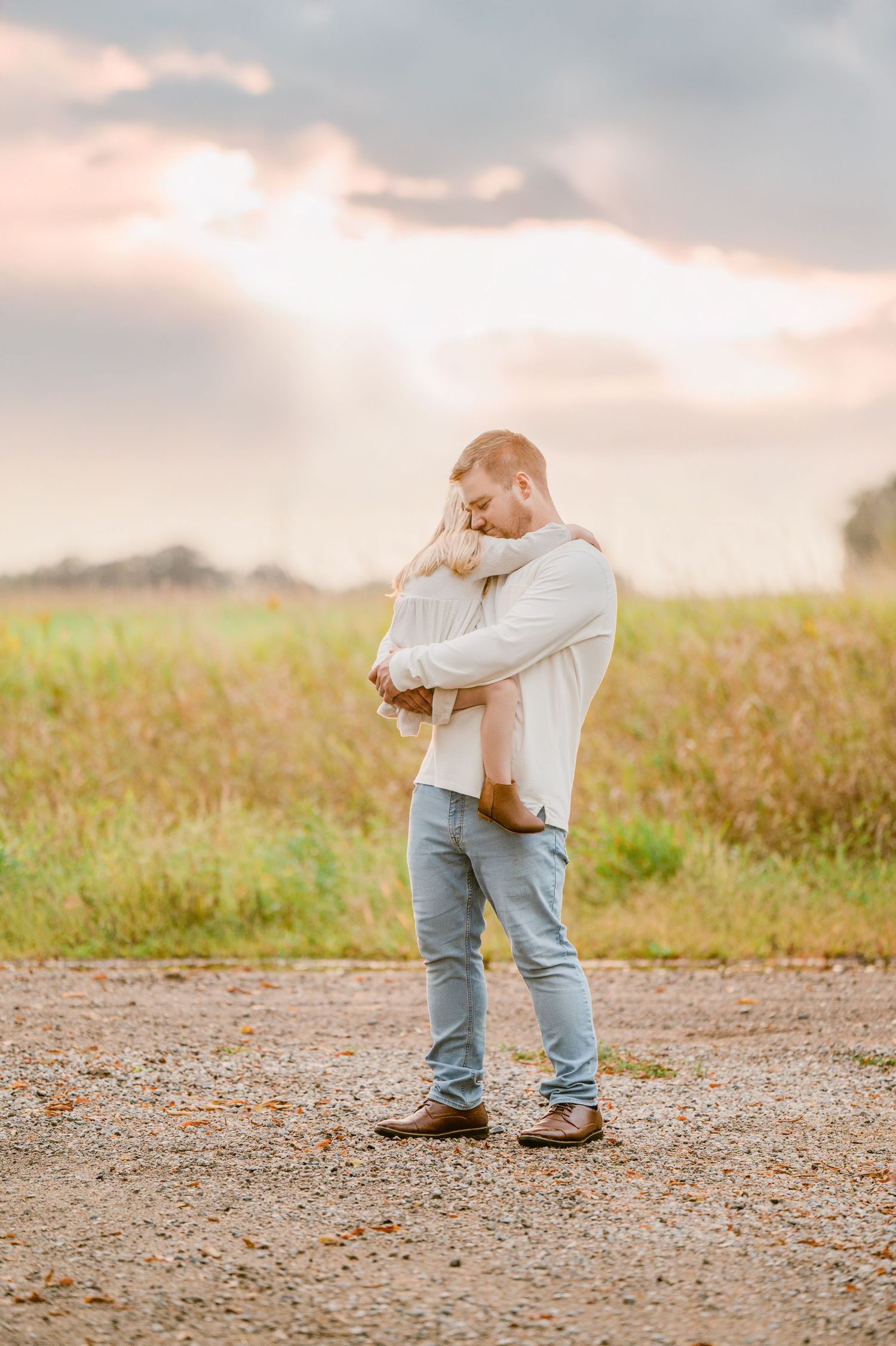 A tender moment captured at sunset as two people embrace on a dirt path surrounded by a golden meadow.