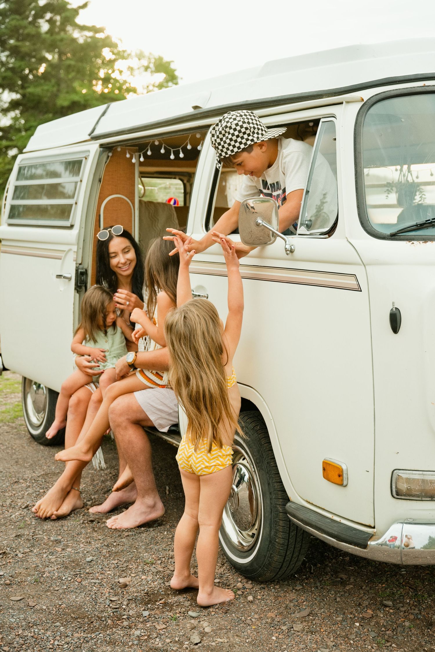 Family enjoying a summer road trip with a vintage white VW camper van, children playing and laughing outside.