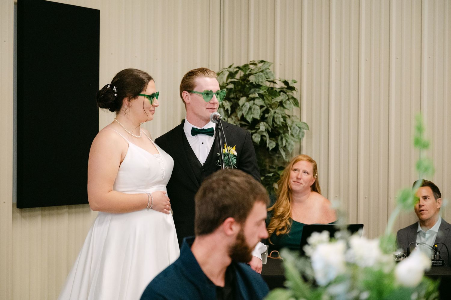 Wedding party members socialize at wooden tables during a casual reception celebration.