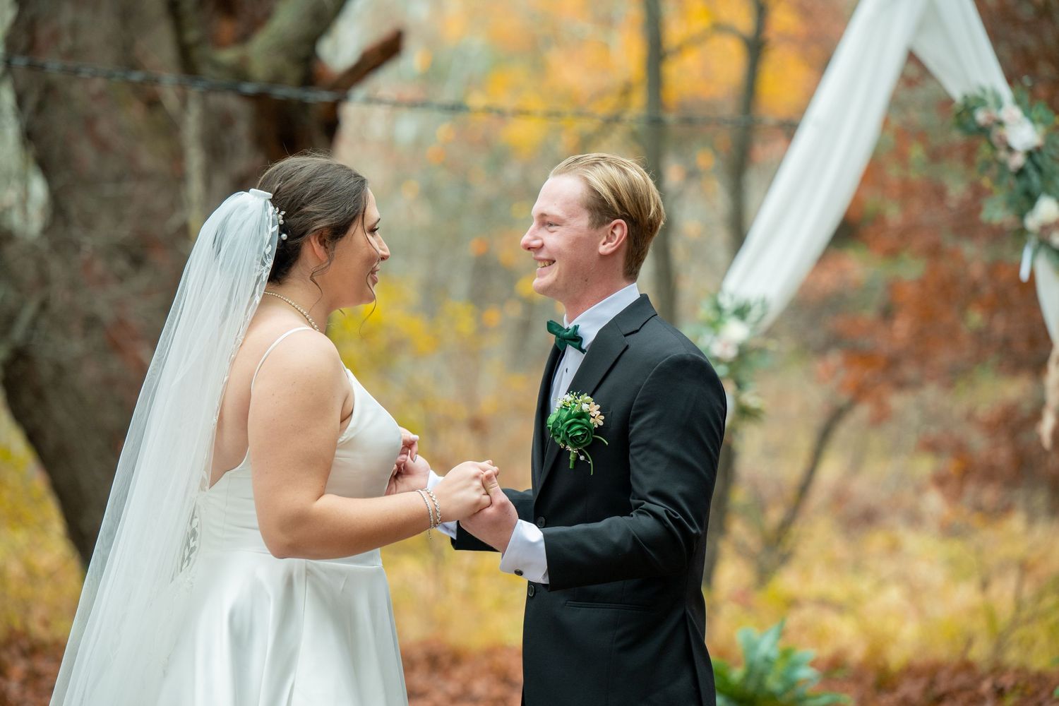 A joyful wedding couple shares an intimate moment outdoors during autumn with colorful fall foliage in the background.