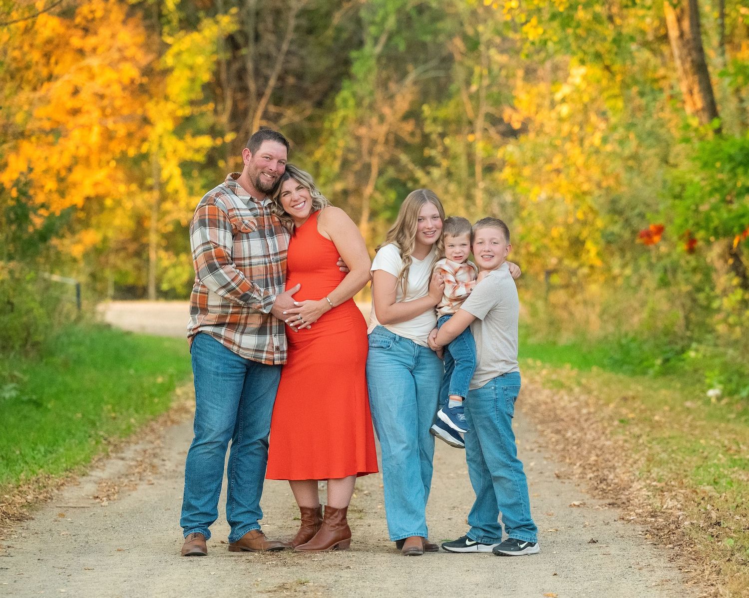 A family poses together on a fall path surrounded by vibrant yellow autumn foliage and trees.
