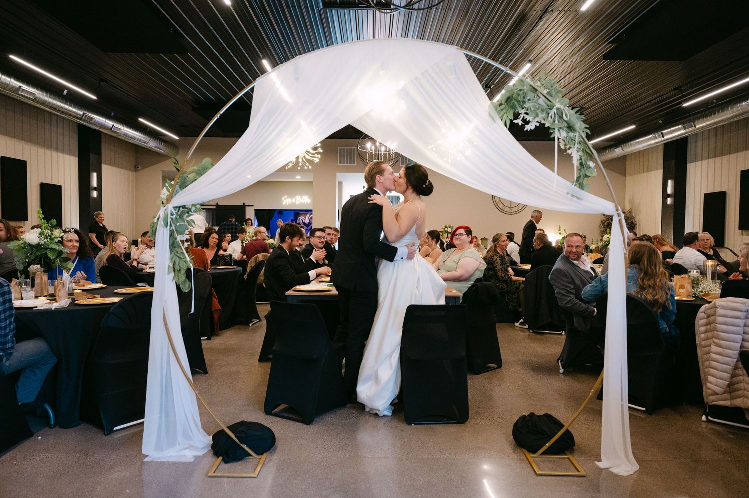 Indoor wedding reception venue decorated with white fabric draping and elegant lighting.